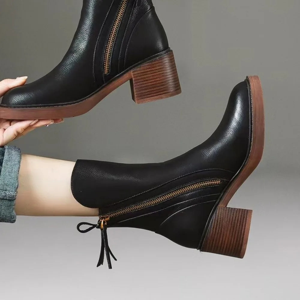 Edith black block heel ankle boots on foot, one held in hand, showing the side zip and tassel pull – Black