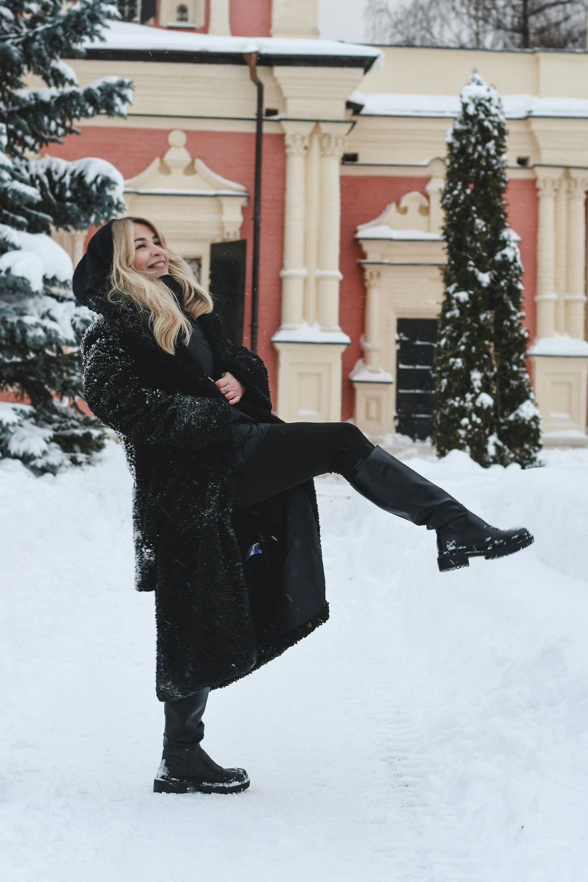 Woman in a long black coat and black knee-high boots in the snow