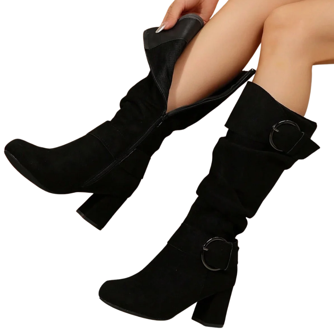 A pair of black knee-high slouchy boots with block heels and circular buckle details, shown on a model's legs against a white background.